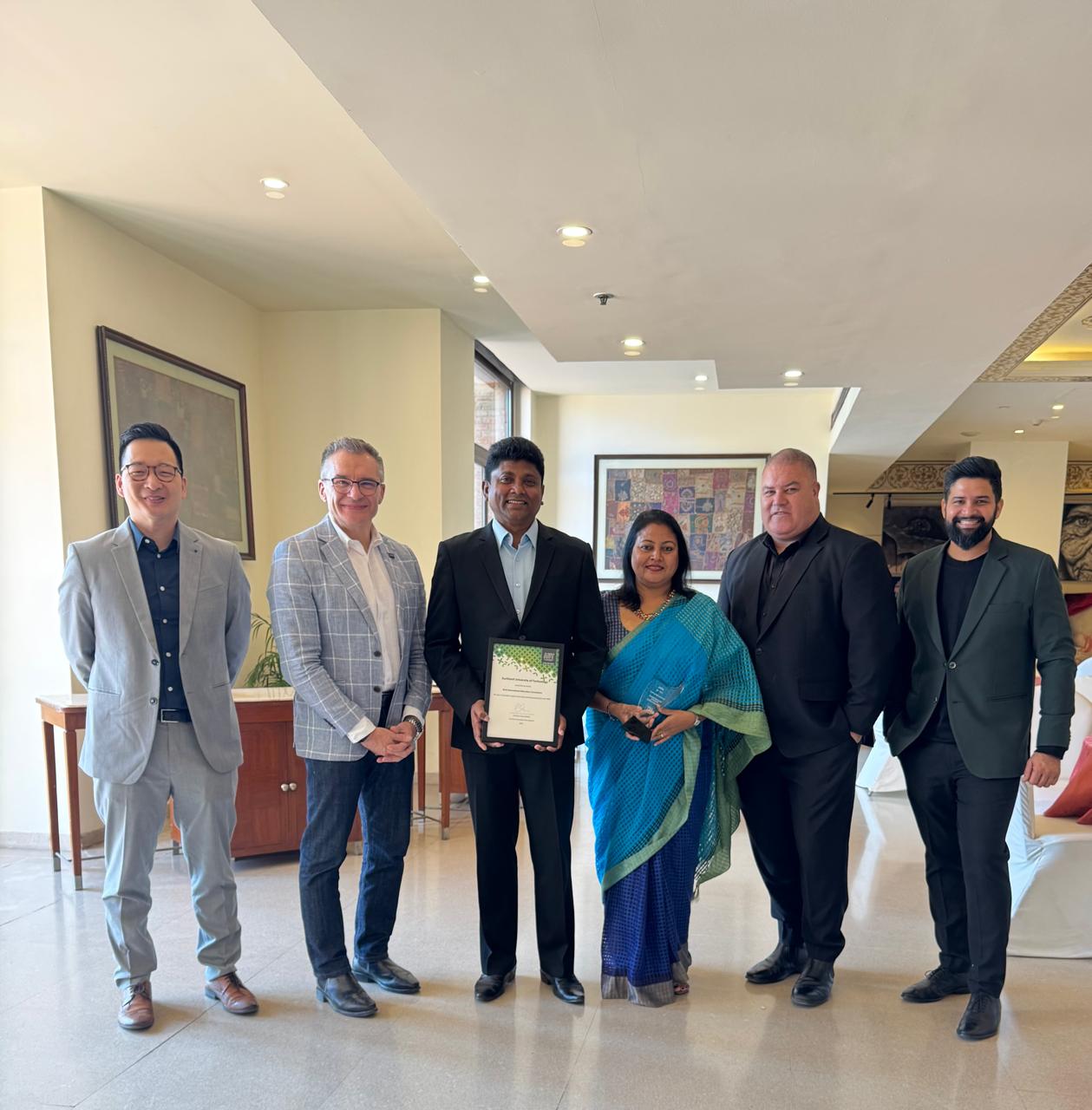 Formal group photograph of six people holding the AUT Best Performing Agent award certificate and trophy in a hotel lobby setting